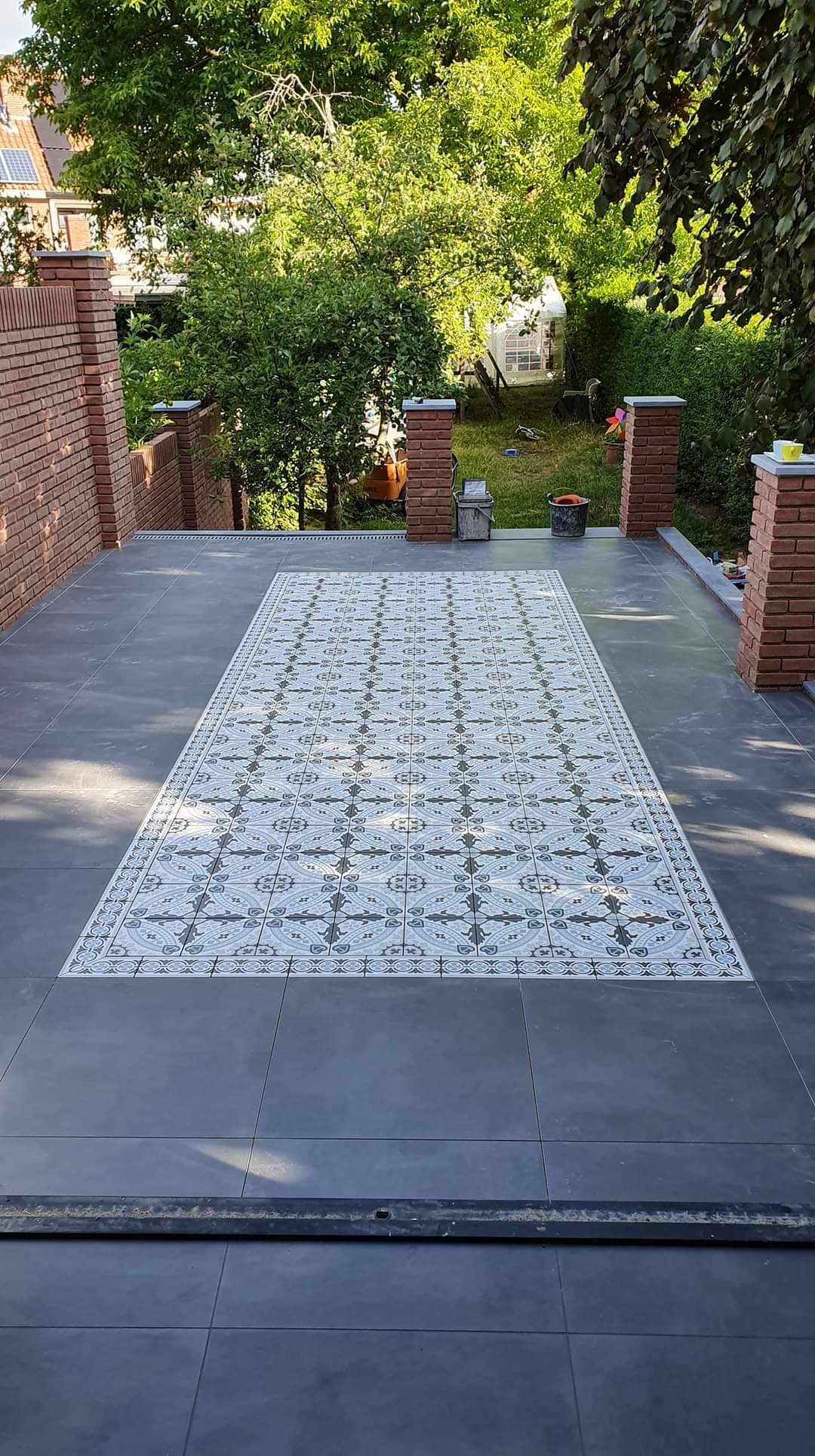 Terras met antraciet tegels en een loper van patroontegels, met tuin op de achtergrond