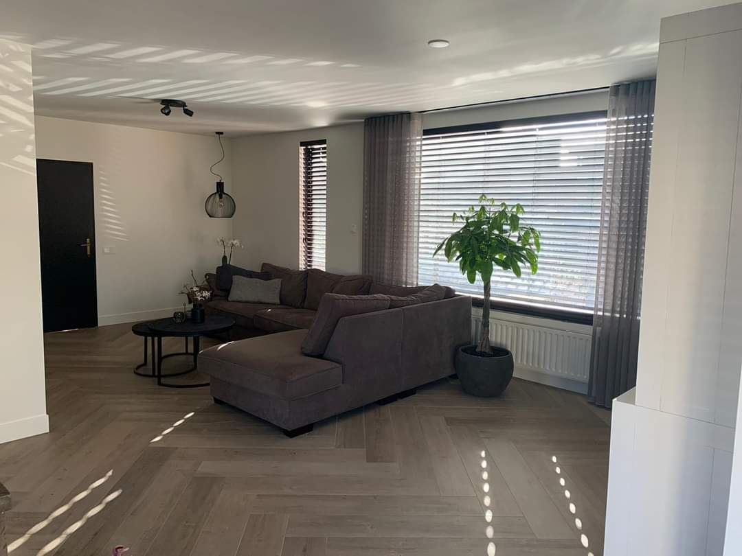 Woonkamer met een visgraat tegelvloer in houtlook en zonlicht door de lamellen