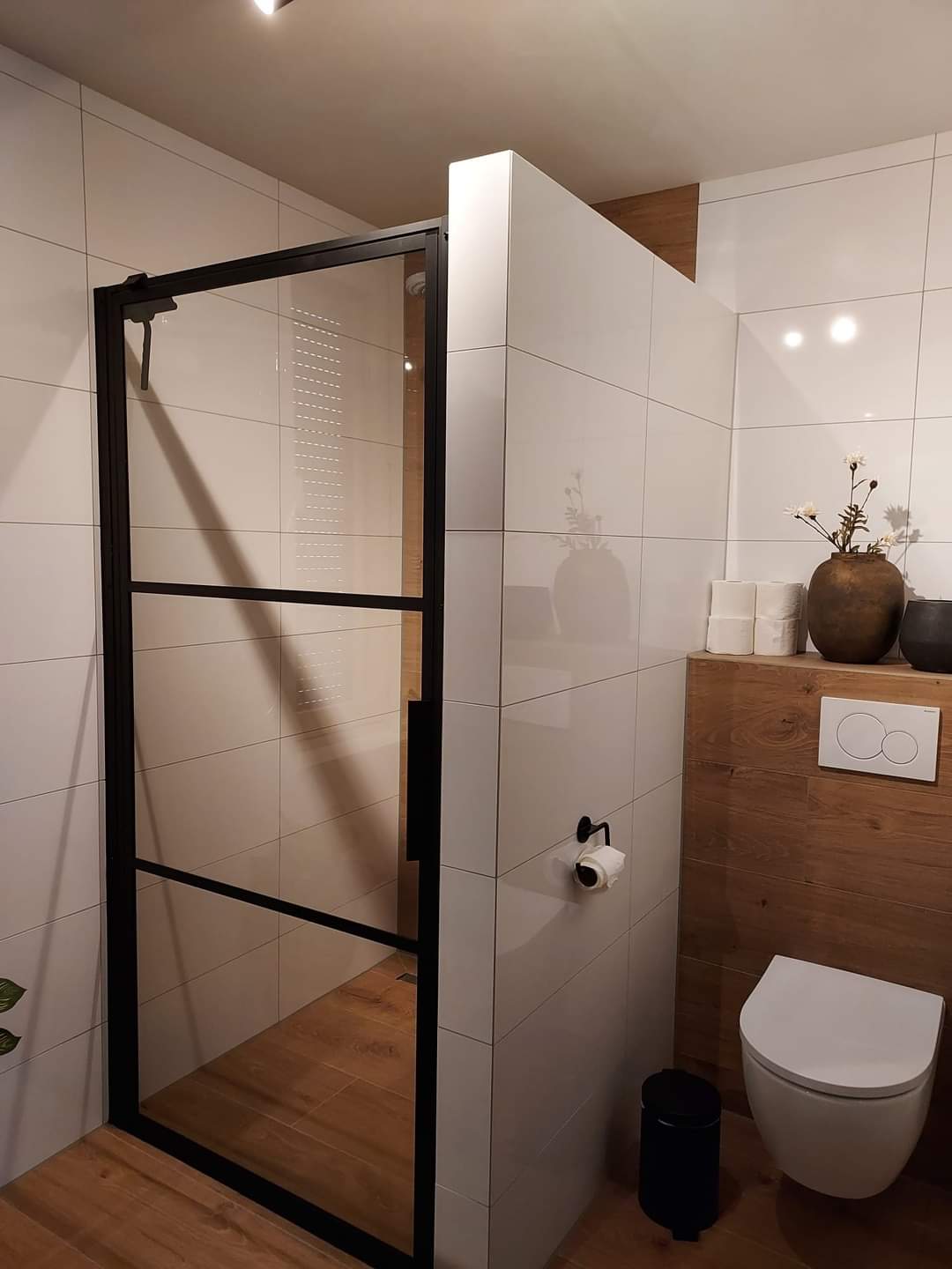 Toilet met hangtoilet tegen een houtlook wand en een douche met zwarte stalen deur